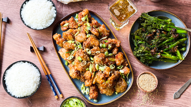 1-wok sesame chicken on serving platter with garnishes, rice bowls, and vegetables