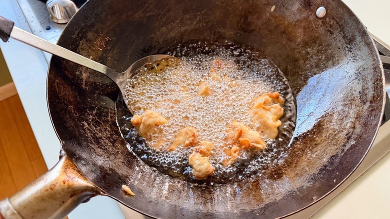 Flash frying battered chicken pieces in peanut oil in wok on stovetop