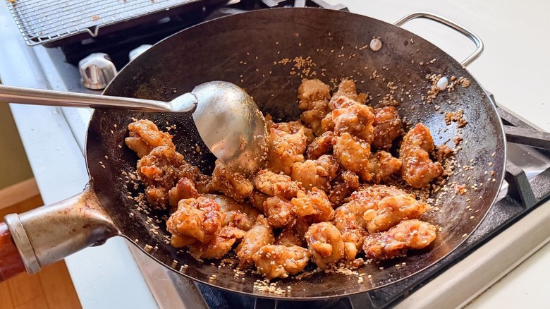 Stirring sesame chicken in wok on stovetop