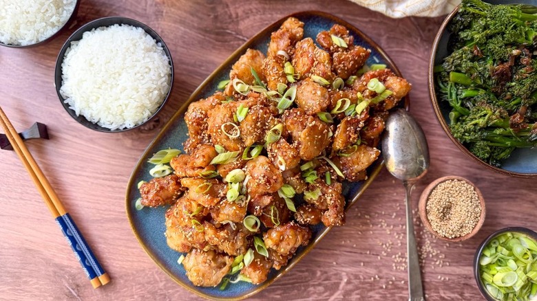 Sesame chicken on serving platter with rice bowls and garnishes