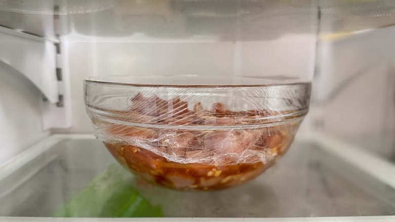 Chicken marinating in glass bowl in refrigerator