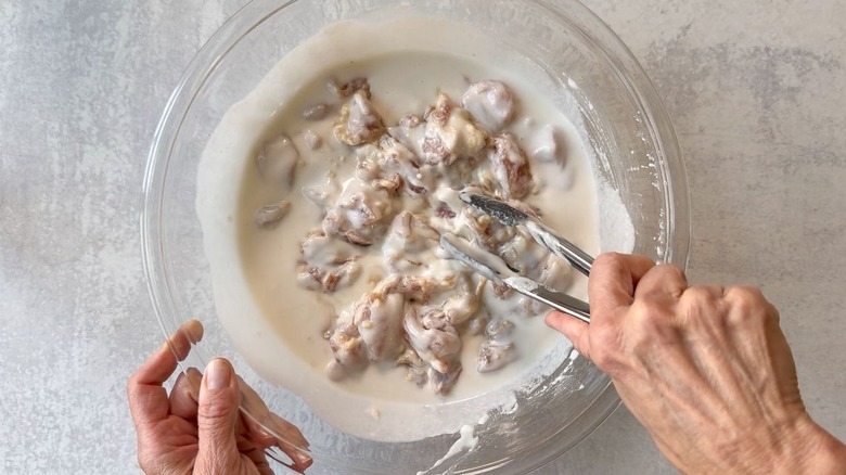 Coating marinated chicken thigh pieces with batter in a large glass bowl