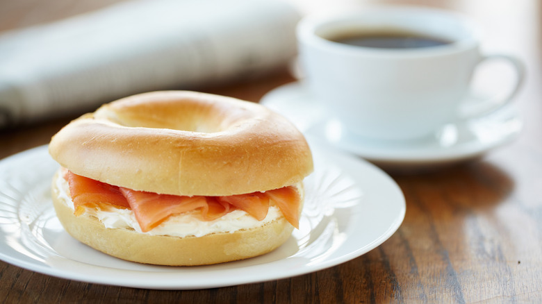 Bagels with cream cheese and lox on white plate with a cup of coffee