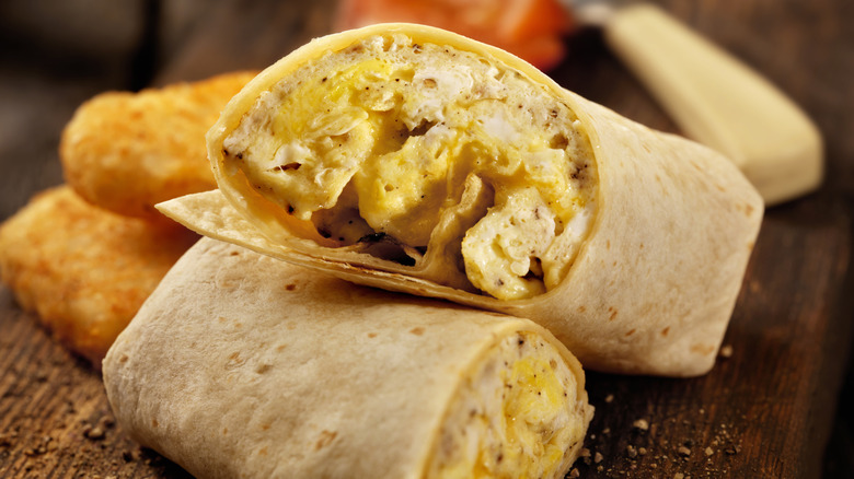 Egg and cheese breakfast burrito sliced in half on wooden cutting board