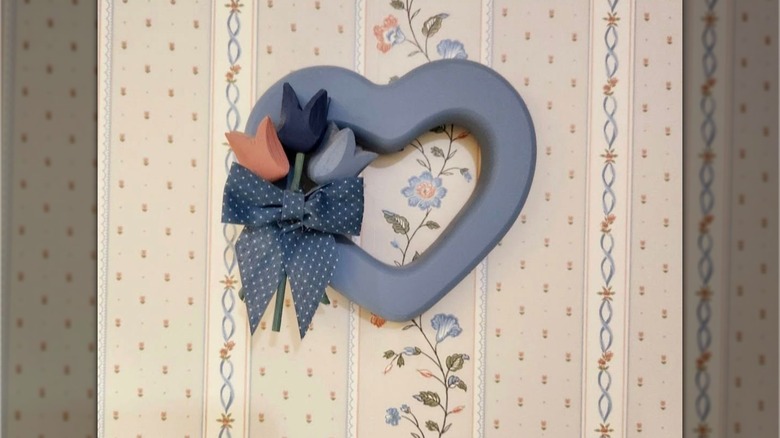Country blue wood heart decoration with a blue and white polka-dotted bow and three wood tulips in front of flowered wallpaper