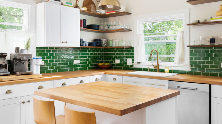Kitchen with wood butcher block countertops, green tile backsplash, and white cabinets