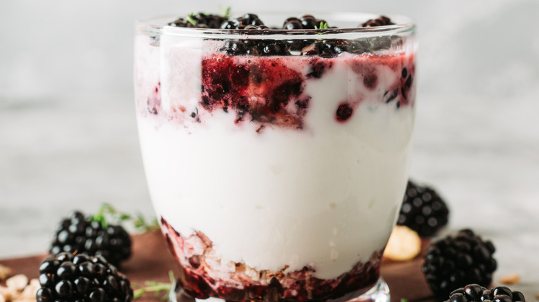 berry parfait in a glass cup sitting on a counter surrounded by blackberries