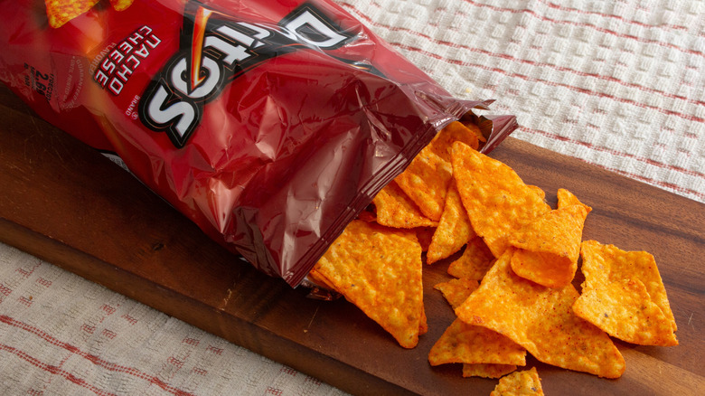 Bag of Doritos chips laying across a wood serving board atop white and red dish towel.
