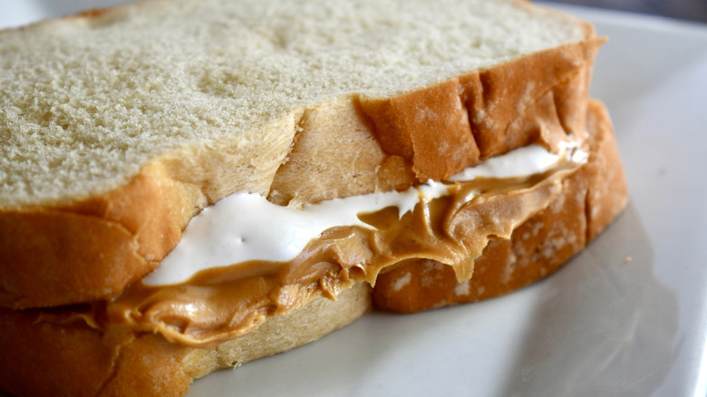 Peanut butter and marshmallow fluff sandwich on white plate.
