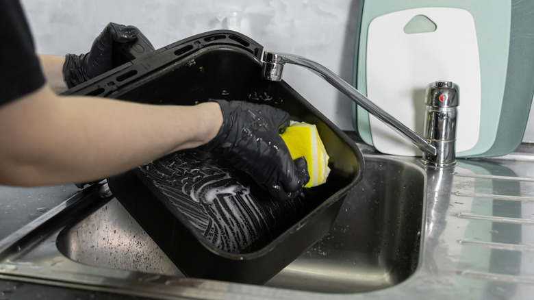 Person cleaning air fryer basket at a kitchen sink