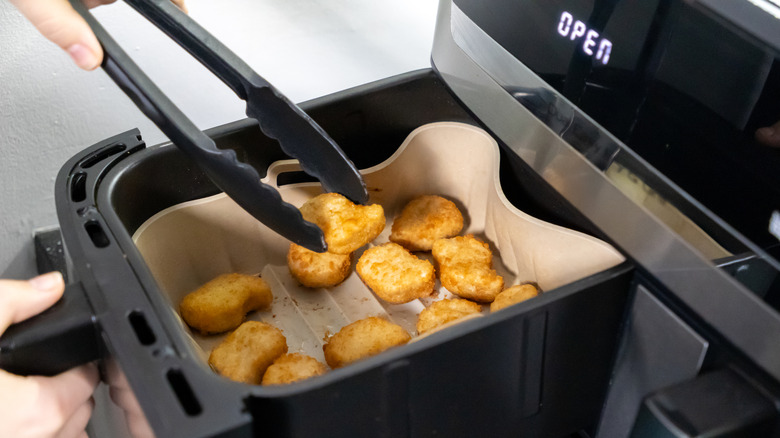 Person cooking chicken nuggets in air-fryer basket