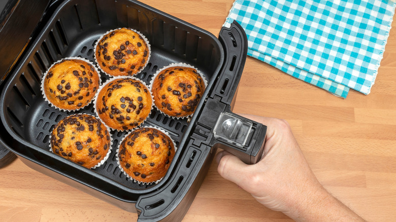 Air fryer basket of chocolate chip muffins being pulled out of appliance by hand