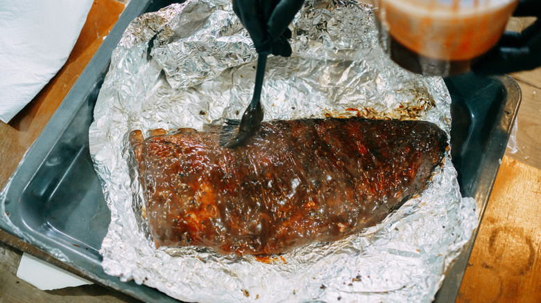 hand brushing meat with sauce in foil