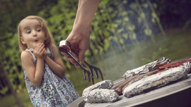 child watching wrapped objects getting cooked on grill