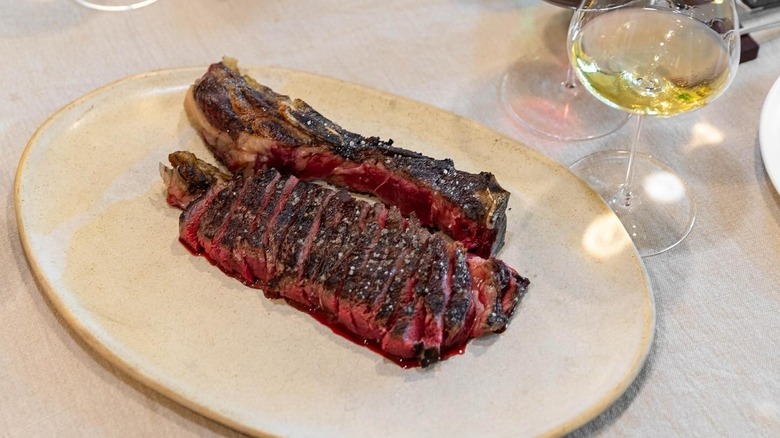 A grilled steak on a plate at Etxebarri next to a glass of white wine