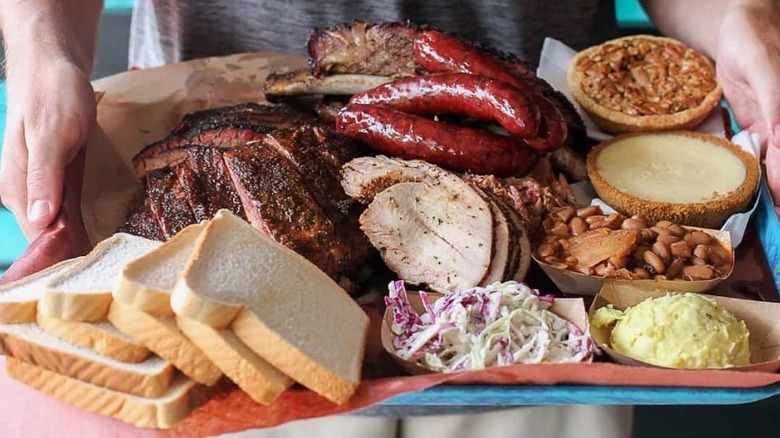 A person holding a tray of barbecue dishes from Franklin Barbecue