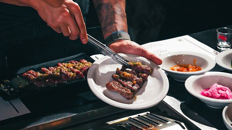 A person placing grilled beef on a plate at Park's BBQ
