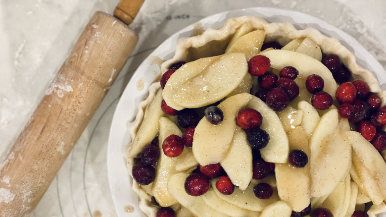 Cranberries on top of apple pie with rolling pin