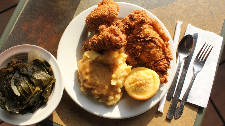 Plate of fried chicken, mashed potatoes, cornbread, and collard greens on a table