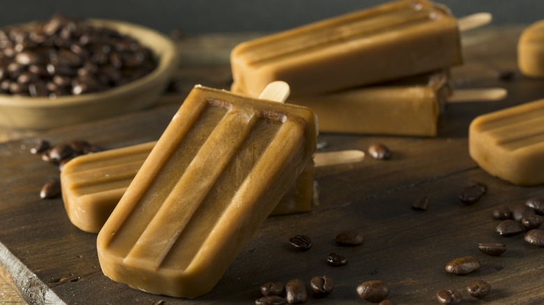 Coffee popsicles on wooden cutting board with fresh beans in background.