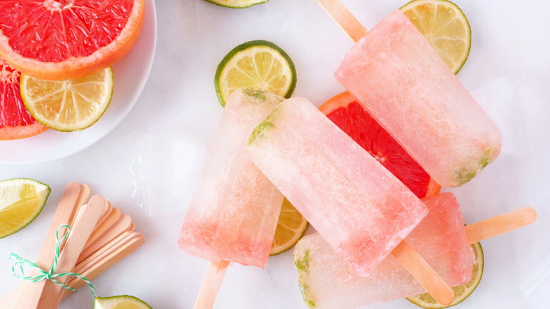 Grapefruit and lime popsicles atop white plate and white counter with bundle of popsicle sticks in left corner.