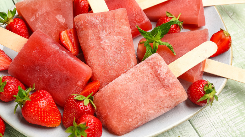 Strawberry popsicles with fresh strawberries on white plate.