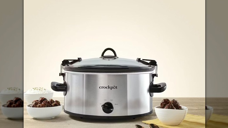 Stainless steel slow cooker with bowls of food surrounding it