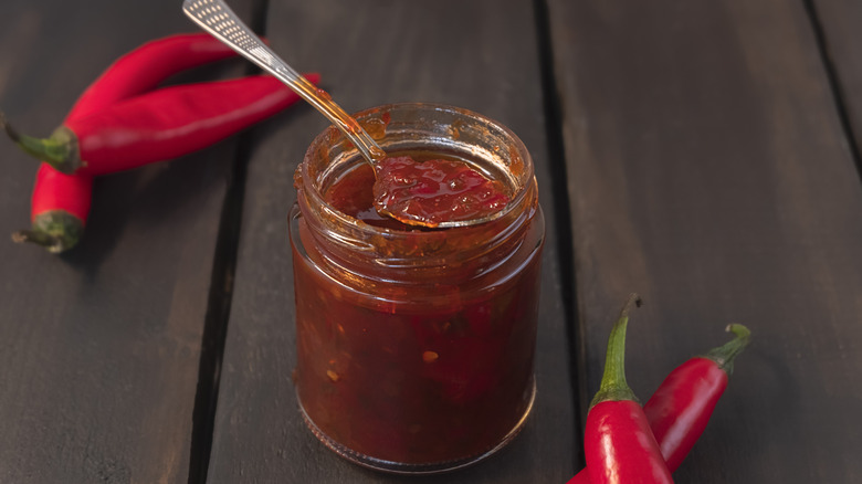 spicy pepper jam on a wooden surface with red chilis