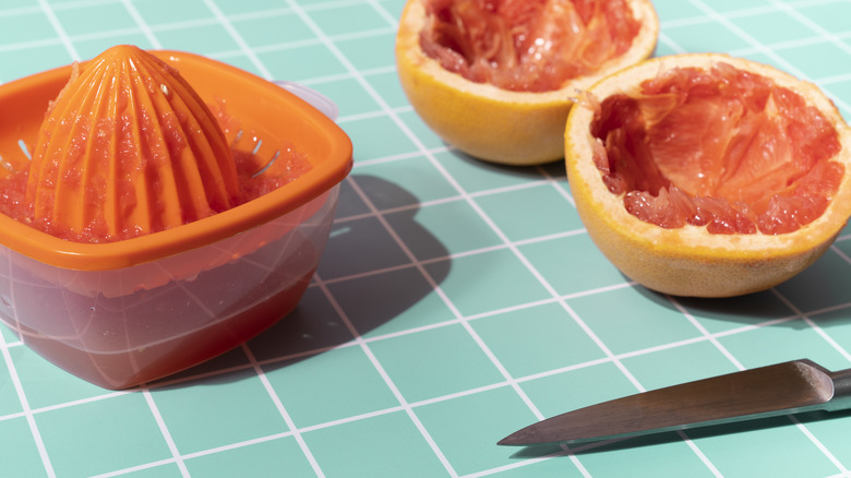 A hand juicer, two juiced grapefruit halves, and a knife sit on a turquoise-tiled table