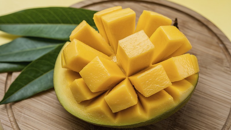 A cross-section of a mango sliced into cubes on a wooden cutting board