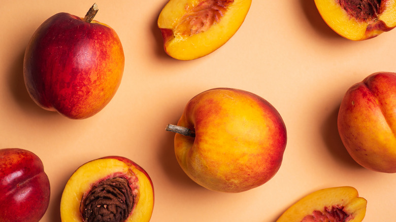 Several peaches, some whole and some cut, arranged on a salmon-colored background
