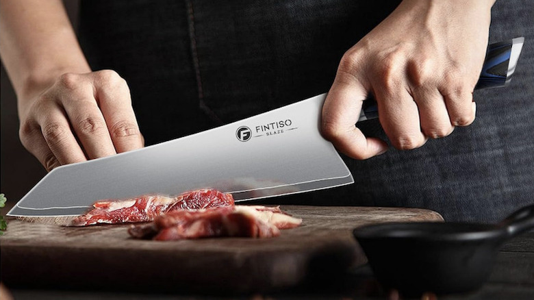 Close-up of a person using a Fintiso 8-inch chef knife to slice meat on a cutting board