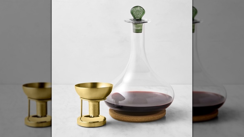 A decanter with a narrow mouth and a wide body and a gold aerator.