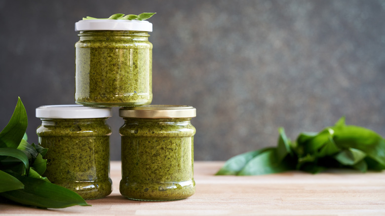 Three jars of pesto with basil leaves alongside