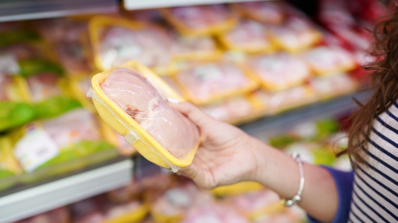 A customer holds packaged raw chicken at the grocery store