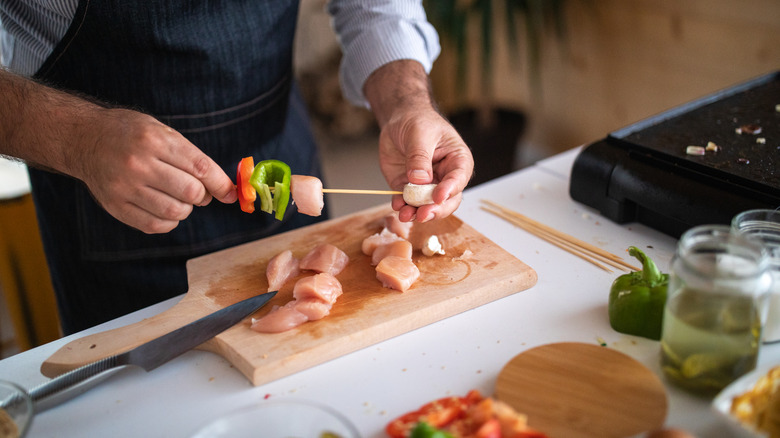 A chef skewers raw chicken and veggies