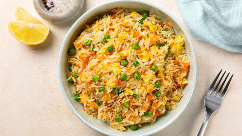Top view of a bowl with fried rice with egg and vegetables, onion, bell pepper, carrot, green peas
