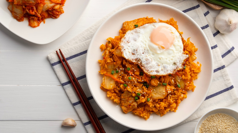 Kimchi fried rice with pork topped with fried egg and sesame seed in white plate
