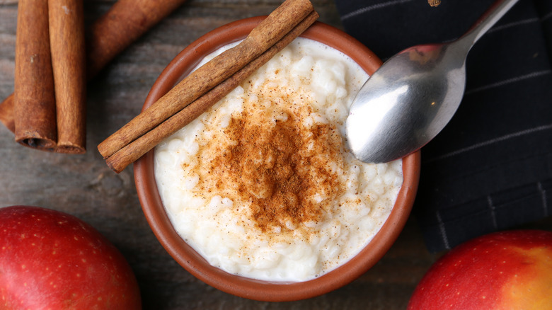 Delicious rice pudding with cinnamon sticks and apples on wooden table, flat lay