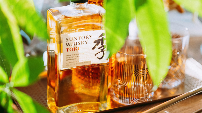 A bottle and glasses of Suntory Whisky amongst some leaves