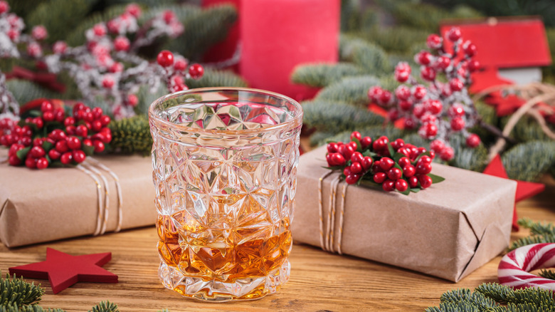 A hand reaches for a glass of Scotch on the rocks with Christmas decorations in the background