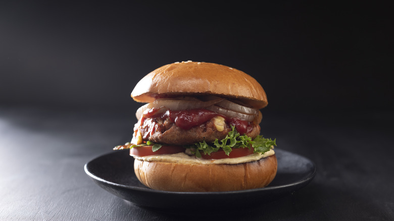 Hamburger with red sauce, onions, lettuce, and tomatoes on a black plate