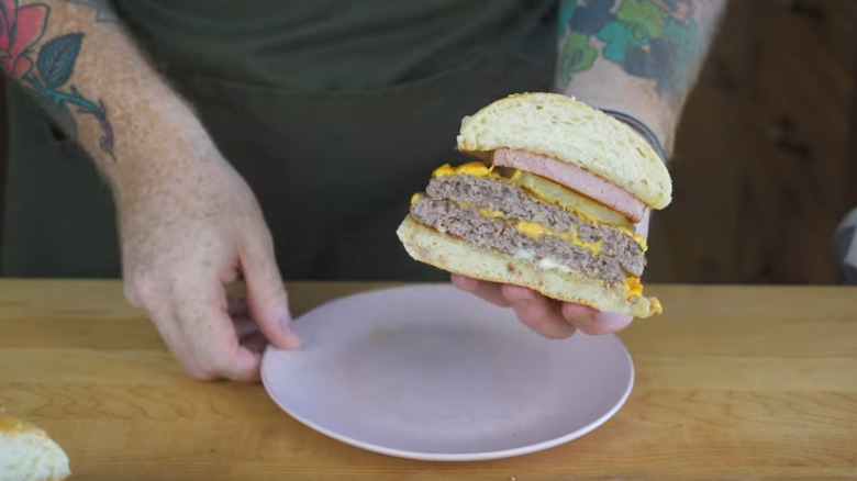 Person holding a hamburger with Spam, cheese, and pickles