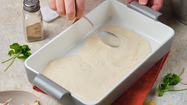 A person spreading béchamel sauce in a baking dish