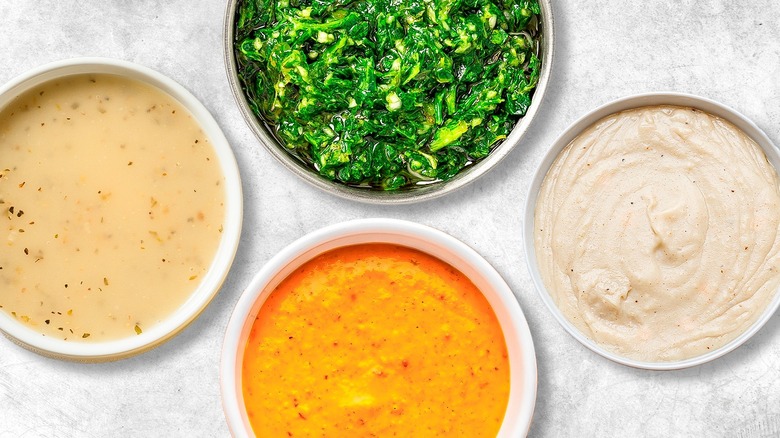Four bowls containing chimichurri, béchamel, romesco sauce, and vinaigrette