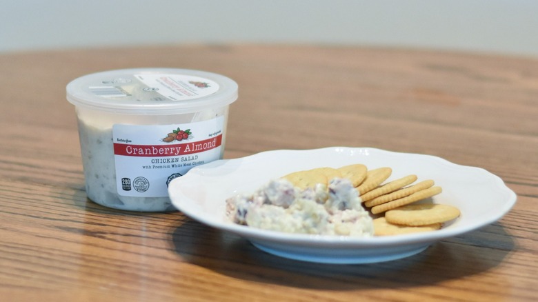 A container of cranberry almond chicken salad next to a white plaate with chicken salad and crackers