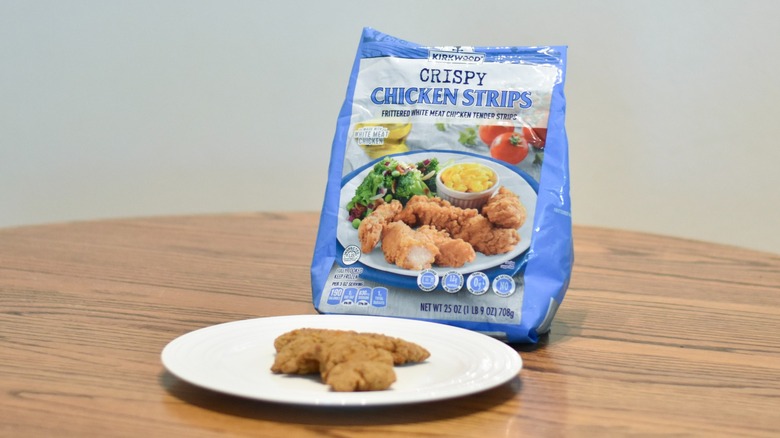 A bag of crispy chicken strips next to a white plate of prepared chicken strips
