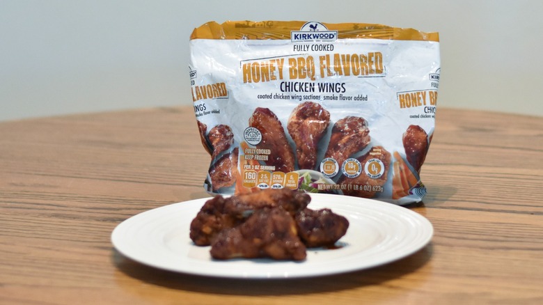 A bag of honey BBQ chicken wings next to a white plate of prepared wings