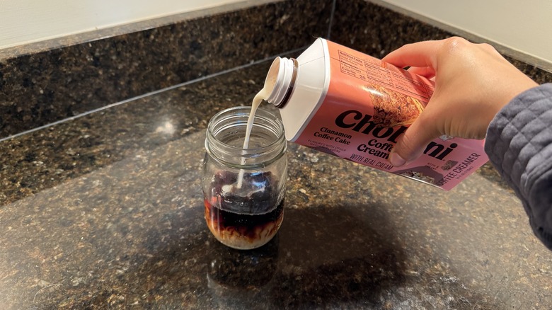 Person pouring coffee creamer into glass of cold brew