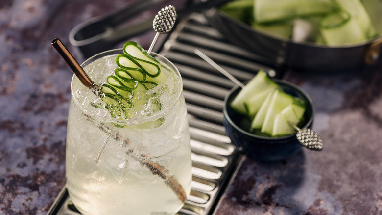 Cucumber gimlet cocktail on a table with cucumber slices in bowls on the side